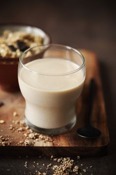 two glasses of milk on a cutting board with spoons and oats in the background