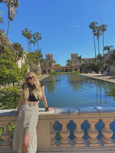 a woman standing next to a pool with palm trees in the background