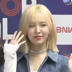 a girl with blonde hair and bangs is holding her hand up