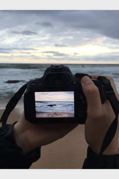 a person holding up a camera to take a photo on the beach with waves in the background