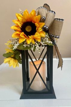 a sunflower and burlap ribbon sits in a lantern with a lit candle