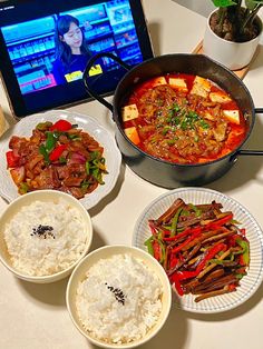 a table topped with plates of food next to a laptop computer and bowl of rice