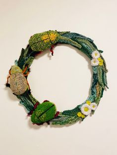 a knitted wreath with flowers and leaves hanging from it's sides on a white wall