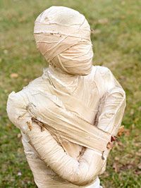 a young boy dressed as a ghost standing in the grass with his arms folded up