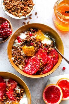 two bowls filled with granola, yogurt and blood orange slices on a table