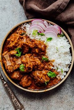 a bowl filled with rice, meat and onions next to a fork on the side