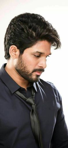 a man in a black shirt and tie looks down at his cell phone while standing against a white background