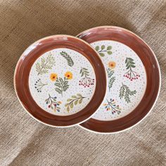 two brown and white plates sitting on top of a cloth covered tablecloth next to each other