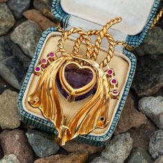 This vintage 14K yellow gold pendant is suspended from an 18K yellow gold chain finished with a 14K yellow gold spring ring clasp. The pendant is centered with one (1) heart mixed cut natural amethyst set into a three-prong setting. The center stone is bordered to each side by three (3), prong set, round mixed cut natural rubies. The pendant measures 56.7mm X 33.2mm. The serpentine style neck chain measuring 24 inches in length. The pendant necklace shows a soft patina. Heirloom Yellow Gold Jewelry For Valentine's Day, Victorian Yellow Gold Jewelry With Large Pendant, Antique Heart-shaped 14k Gold Necklace, Antique Yellow Gold Necklaces For Valentine's Day, Victorian 14k Gold Jewelry For Valentine's Day, Collectible Heirloom Necklace For Valentine's Day, Collectible Yellow Gold Necklace With Heart Charm, Antique Yellow Gold Heart Cut Jewelry, Victorian Yellow Gold Jewelry For Valentine's Day