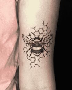 a black and white photo of a bee tattoo on the right arm, with honeycombs in the background