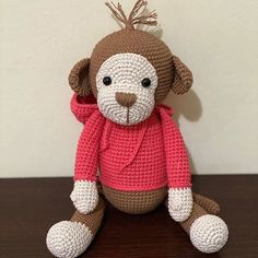 a crocheted monkey sitting on top of a wooden table next to a white wall