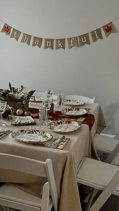 the table is set for thanksgiving dinner with plates and silverware on it, along with an autumn banner