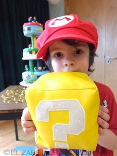 a young boy wearing a mario hat and holding up a paper bag with the letter p on it