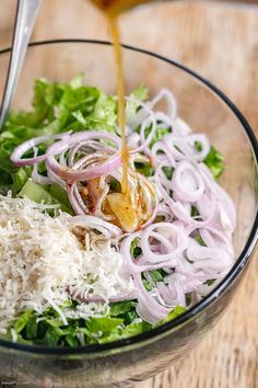 someone pouring dressing into a salad with onions and lettuce in a glass bowl