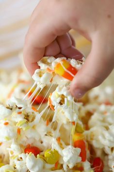 a person is scooping popcorn into a bowl with candy corn and marshmallows