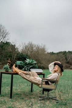 a woman sitting on top of a chair next to a table in the middle of a field