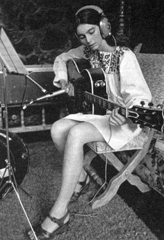 a woman with headphones sitting on a bench playing an acoustic guitar