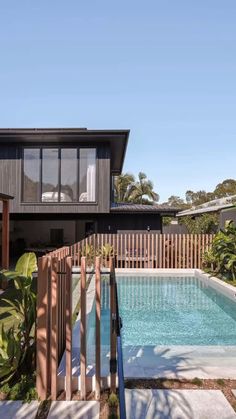 an outdoor swimming pool in front of a house with wooden fence and trees around it