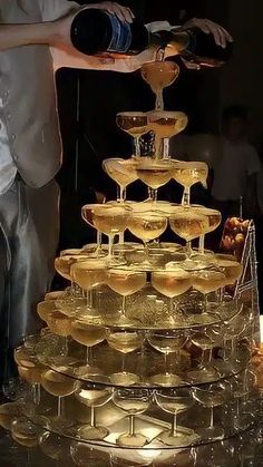 a man pouring wine into glasses on top of a cake stand that is filled with champagne