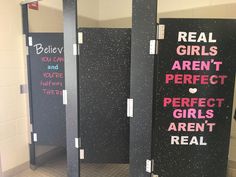 three black stalls with pink writing on them in a public restroom, one is for real girls and the other says aren't perfect girls aren't real