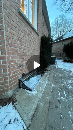 a window on the side of a brick building with snow on the ground in front of it