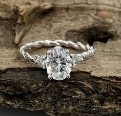 a white gold engagement ring with diamond accents on top of a piece of drift wood