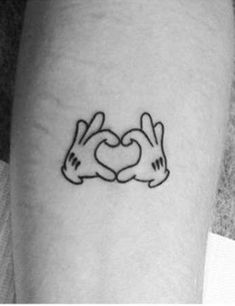 two hands making a heart tattoo on the left inner arm, with one hand in the shape of a heart