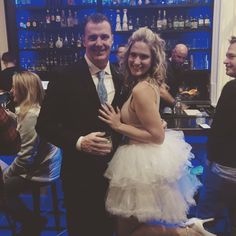 a man standing next to a woman in a tutu at a bar with other people