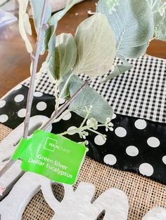 a table topped with a vase filled with flowers and greenery next to a sign that says green silver dollar eucalyptus