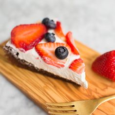 a piece of cheesecake with strawberries and blueberries on top is sitting on a wooden cutting board