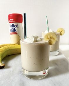 two smoothies with bananas and whipped cream are on a table next to a bag of buttered milk