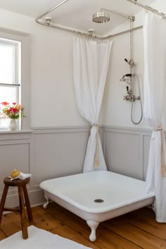 a white bath tub sitting under a window next to a wooden floor covered in curtains