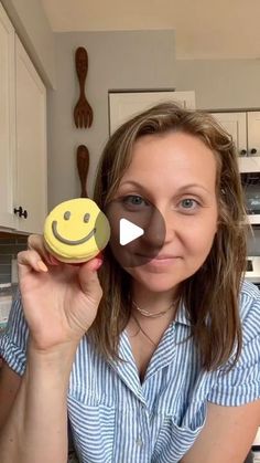 a woman holding up a cookie with a smiley face on it in front of her face