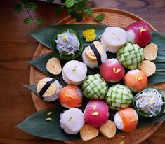 a wooden plate topped with different types of sushi on top of green leafy leaves