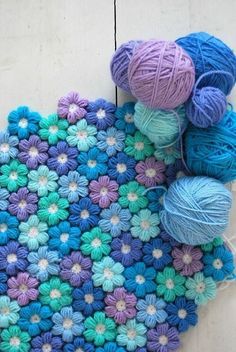 several balls of yarn sitting on top of a crocheted mat with flowers in the middle