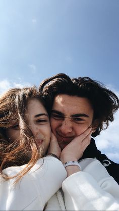 a man and woman standing next to each other with their hands on their cheeks, looking at the camera