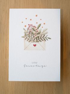 a card with an envelope and flowers in it on top of a wooden table next to a pen