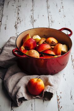 an old red pot filled with apples on top of a wooden table next to a cloth