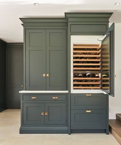 a wine cellar in the middle of a kitchen with dark green cabinets and white counter tops