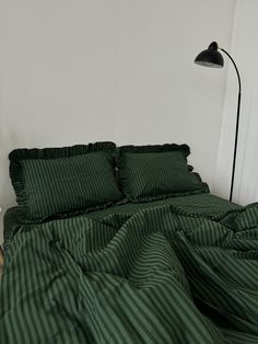 a bed with green sheets and pillows in a white room next to a black lamp