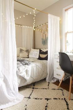 a bedroom with white drapes and string lights on the ceiling, along with a black chair