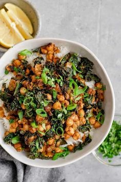 a white bowl filled with rice, beans and greens next to sliced lemon wedges