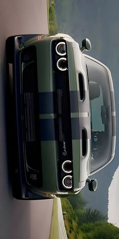 the front end of a green and white car hanging from a wall next to a body of water