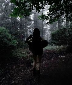 a woman walking in the woods at night with her back turned to the camera,