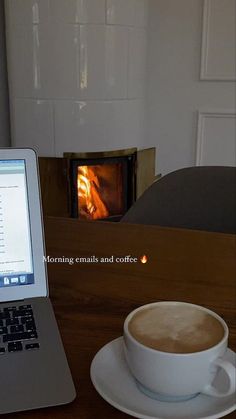 an open laptop computer sitting on top of a wooden table next to a cup of coffee