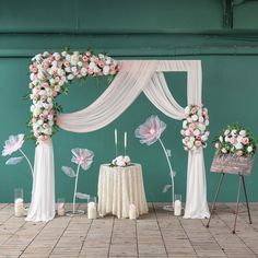 a table with flowers and candles on it in front of a green wall decorated with white drapes