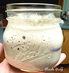 a hand holding a mason jar filled with liquid and sprinkled on the lid