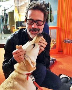 a man sitting on the floor petting a dog with his mouth open and tongue out