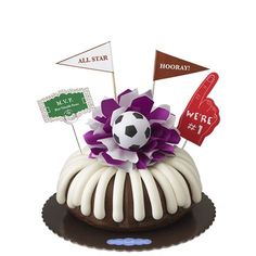 a cake with white icing and purple flowers on top is decorated with flags and a soccer ball