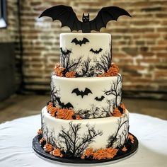 a three tiered cake decorated with bats and flowers on a table in front of a brick wall